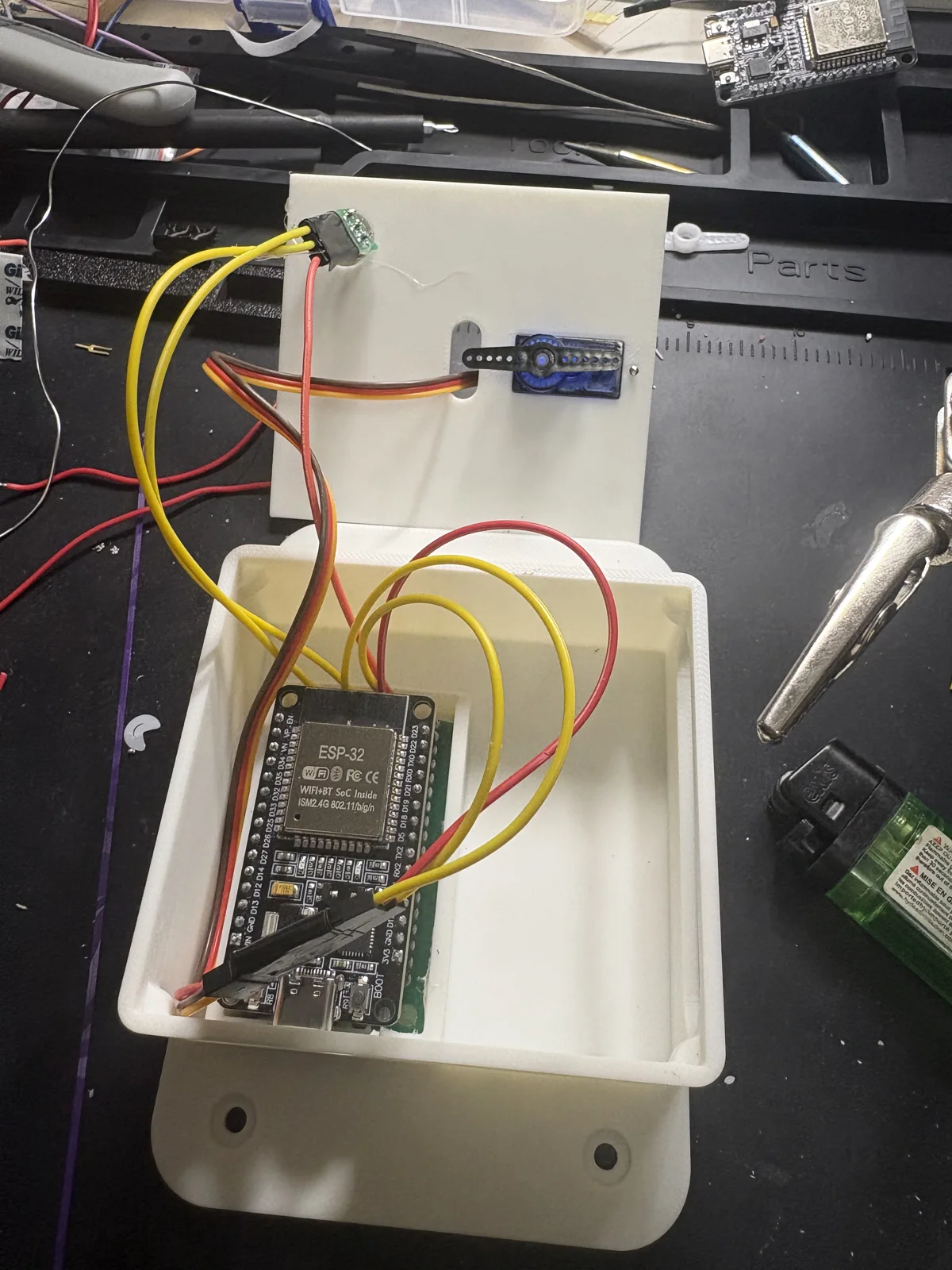 Wiring the ESP32, PIR, and servo into the printed enclosure on the bench.