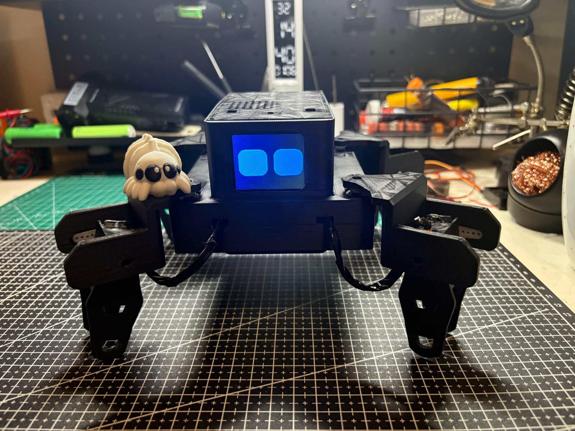 Momo, a four-legged robot with an animated blue face, on Eben's workbench